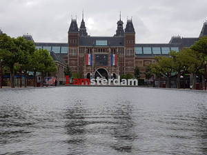 阿姆斯特丹博物館建築，配有水景和 I amsterdam 標誌 — 湯姆·霍蘭德 壁紙