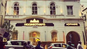 歷史悠久的白色建築，帶有 Higginbothams 標誌和繁忙的街景。 — 清奈 壁紙
