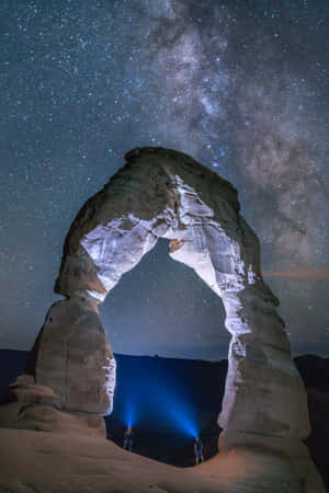兩人在星空下，銀河可見，站在發光的石拱門下。 — 魔法森林 壁紙