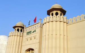 藍天下帶有旗幟和圓頂塔樓的巴基斯坦政府建築 — 巴基斯坦國旗 壁紙
