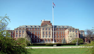 大型大學建築，帶有旗桿和綠色草坪，在陽光明媚的日子裡。 — 酷 壁紙