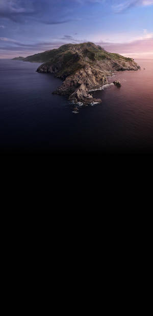黃昏時分的岩石島嶼，平靜的海水和紫粉色的天空 — macOS Catalina 壁紙