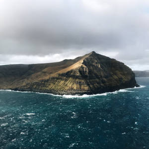 灰色天空下暴風雨海洋中的崎嶇懸崖島嶼 — 法羅群島 壁紙