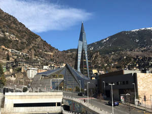 山城中的現代玻璃建築，背景有白雪覆蓋的山峰和下方的道路。 — 城市 壁紙