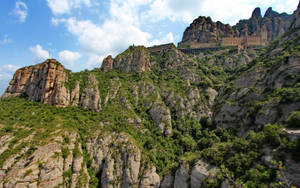 修道院坐落在岩石山上，被綠色植物覆蓋，藍天白雲下。 — 山景 壁紙