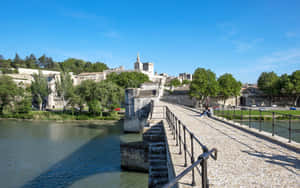 藍天下橫跨河流的石橋，周圍有歷史建築和樹木 — 湖泊 壁紙