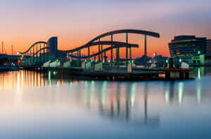 日落時分水面上的現代拱橋，城市燈光倒映。 — MacBook Air 壁紙