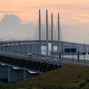 汽車在日落時分駛過一座大橋，水面上有一艘貨船。 — 海洋 壁紙