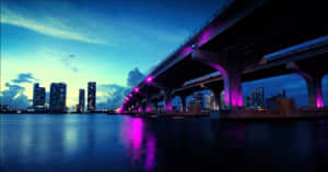 紫色燈光橋樑橫跨水面，背景為暮色中的城市天際線。 — Chill 壁紙