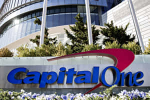 Capital One銀行標誌，背景有藍色花朵和玻璃建築。 — 花 壁紙