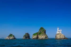 藍色海洋和清澈天空下岩石島上的白色燈塔