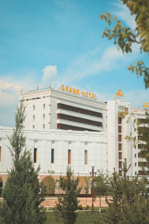 藍天下被綠樹環繞的帶有金色招牌的Grand Hotel建築。 — 烏茲別克 壁紙