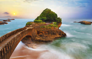 日落時分，石橋越過海浪通往一個樹木覆蓋的島嶼。 — 海景 壁紙