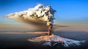 一座積雪火山在日出時噴發，伴隨著巨大的火山灰雲。 — 自然 壁紙