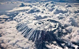 一座積雪覆蓋的火山，其火山口從上方穿透雲層。 — 山脈 壁紙