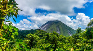在部分多雲的天空下，一座高聳的綠色火山被茂密的叢林包圍。 — 薩爾瓦多 壁紙