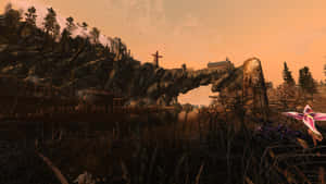 夕陽下，一座木橋穿過石拱門，拱門上方的懸崖上有城堡和風車。 — 上古卷軸V：無界天際 壁紙