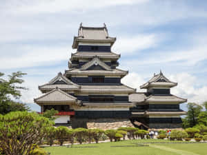 一座歷史悠久的日本城堡，擁有層疊屋頂和石質地基，周圍環繞著修剪整齊的綠植，天空多雲。 — 花園 壁紙