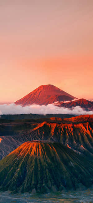 火山山脈沐浴在日落橙色光芒中，下方有雲層。 — 自然 iPhone 壁紙