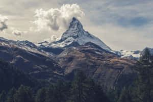 在多雲的天空下，積雪的山峰從森林覆蓋的山坡上拔地而起。 — 雲朵 GIF 壁紙