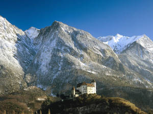 山坡上的城堡，背景是白雪覆蓋的山脈。 — 惡魔城 壁紙