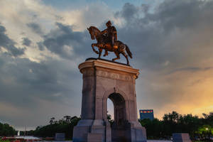 暮色中石拱門上的青銅騎馬雕像，多雲天空和樹木 — 休士頓 壁紙