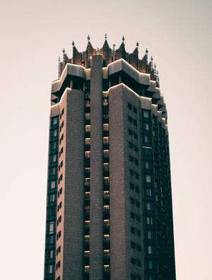 哥德式摩天大樓，窗戶亮著燈光，襯著蒼白的天空 — 地獄客棧 壁紙