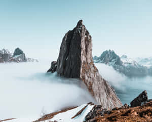 尖銳的山峰從雲中浮現，遠處有雪峰和水面。 — 山脈 壁紙