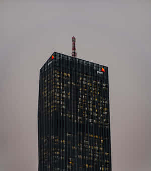 高聳的玻璃辦公大樓，窗戶亮著燈，映襯著暮色天空。 — Vivo X Fold 壁紙