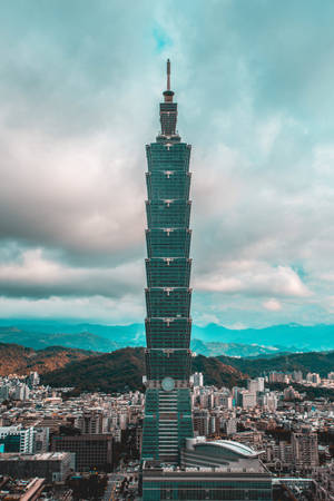 台北101摩天大樓聳立在密集的城市之上，背景有山脈。 — 台灣 壁紙