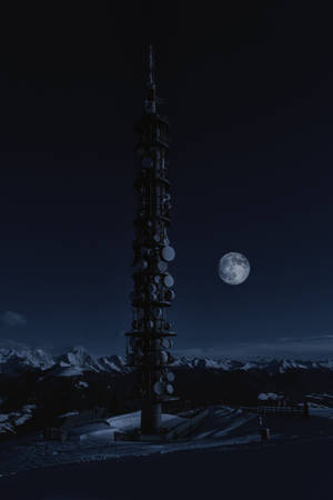 夜間滿月下積雪山上的一座高聳通訊塔。 — 月光 壁紙