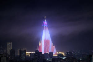 夜晚一座明亮照明的金字塔形建築，背景是城市天際線。 — 地獄客棧 壁紙