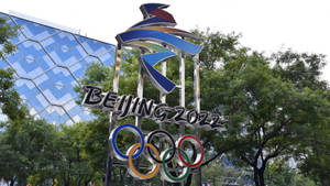 北京2022奧運標誌雕塑，奧運五環被樹木和現代建築環繞。 — 奧運 壁紙