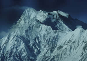 在深藍色天空下，一座雄偉的雪山山峰被雲霧環繞。 — 拉合爾 壁紙