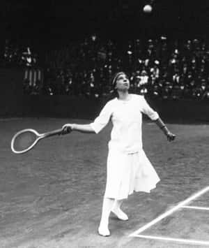 女子穿著1920年代復古服裝在紅土球場上發網球。 — 運動 壁紙