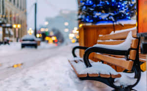 積雪的長凳在積雪的城市街道上，背景有模糊的燈光。 — 冬季風景 壁紙