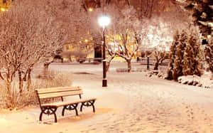 夜晚被路燈照亮的雪地公園長椅，雪地上有腳印。 — 冬季風景 壁紙