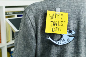 一張黃色便利貼寫著「HAPPY FOOLS' DAY!」，貼在灰色外套上，並有一個紙魚。 — 高飛 壁紙