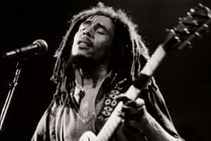 Bob Marley 在舞台上彈吉他並對著麥克風唱歌。 — 巴布·馬利語錄 壁紙
