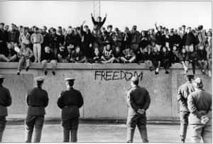 人們坐在帶有「FREEDOM」塗鴉的牆上，士兵站在下方。 — 德國 壁紙