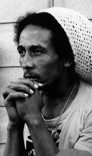 Bob Marley戴著鉤針編織帽，手持香煙，擺出沉思姿勢。 — 巴布·馬利語錄 壁紙