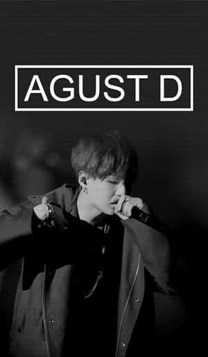 歌手 Agust D 在舞台上手持麥克風表演的黑白照片。 — 赫利希克·羅森 壁紙