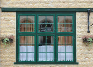黃色磚建築中帶有蕾絲窗簾的綠色窗戶，配有花箱。 — Windows 壁紙