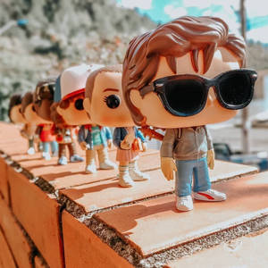 《怪奇物語》的 Funko Pop 人偶在明亮的陽光下排列在磚牆上。 — 怪奇物語 4 壁紙