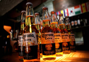 木製酒吧檯上的一排排Corona Extra啤酒瓶，背景有旗幟。 — 啤酒 壁紙