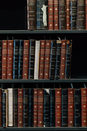 一排排古董法律書籍，深色皮革書脊上帶有金色文字，排列在木書架上。 — 書本美學 壁紙