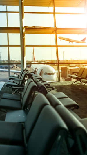 一排排空置的機場座位望向日落時降落的飛機。 — 機場 壁紙