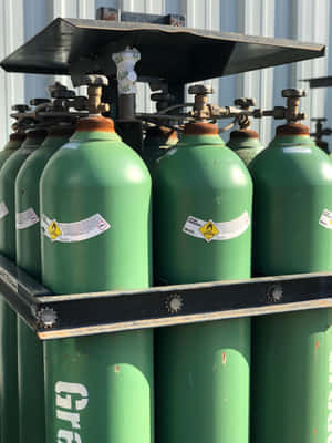 金屬架上的綠色氧氣罐帶有危險標籤 — 瓦斯 壁紙