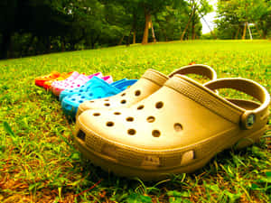 色彩繽紛的Crocs鞋排列在草地上，後面有樹木。 — Crocs 壁紙