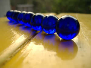 戶外黃色木桌上的一排藍色彈珠。 — 美麗的藍色 壁紙